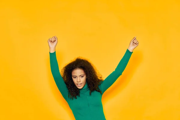 穿着绿色毛衣、高举双手、站在黄色背景上跳舞的女人 — 图库照片