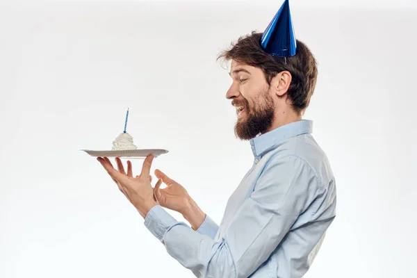Un homme célèbre un anniversaire sur un fond clair avec un gâteau dans une plaque flûte chapeau amusant — Photo