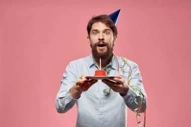 Pastalı ve mavi gömlekli bir adam pembe arka planda doğum günü tatili manzaralı.