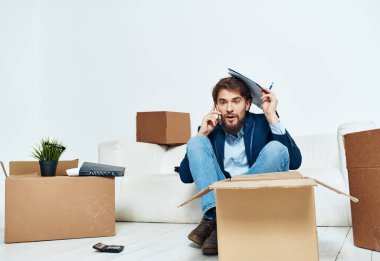 Kutuların yanındaki işadamı eşyaların açıldığı yeni bir ofise taşınıyor. 