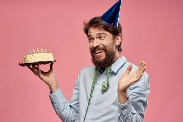 케이크를 접시에 넣고 핑크 배경의 생일 연휴에 파란 셔츠를 입은 남자의 모습 — 스톡 사진