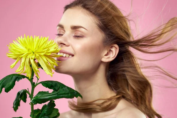 Hermosa chica con una flor amarilla sobre un fondo rosa maquillaje hombros desnudos —  Fotos de Stock