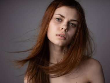 Gri arka planda çıplak omuzlu, kızıl saçlı bir kadının yüzü. Yakın plan modeli.