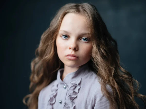 Retrato de uma menina bonita com cabelo encaracolado e um vestido cinza em um fundo escuro — Fotografia de Stock