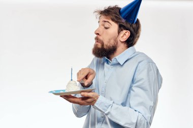 Sakallı bir adam arka planda hafif bir doğum gününde elinde pasta tutuyor.