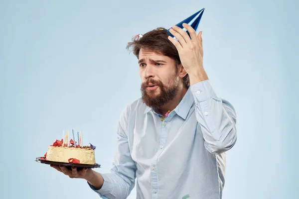 手にケーキと頭にお祝いの帽子をかぶったシャツの男 — ストック写真