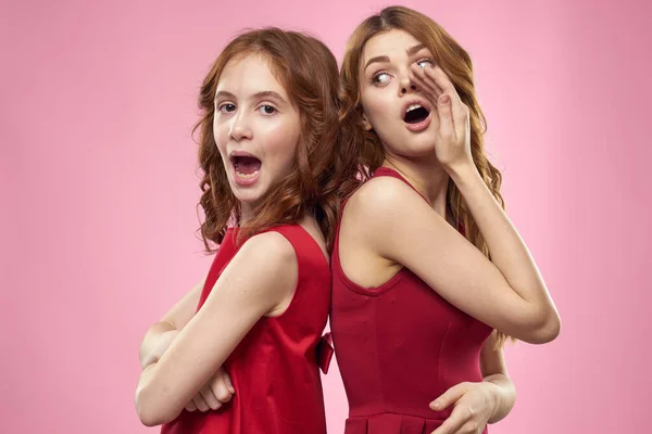 Mutter und Tochter in roten Kleidern umarmt Spaß Fratze Kindheit Freude rosa Hintergrund — Stockfoto