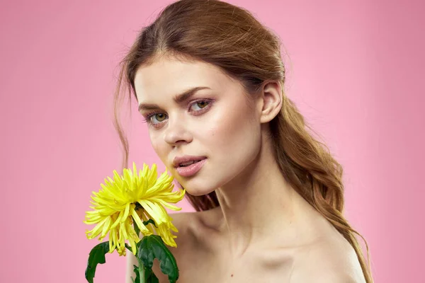 Vacker flicka med en gul blomma på en rosa bakgrund nakna axlar makeup — Stockfoto