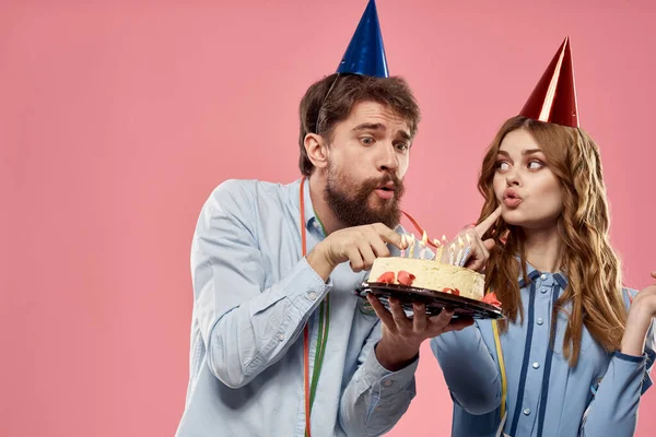 Party muž a žena s dort na růžovém pozadí firemní narozeniny — Stock fotografie