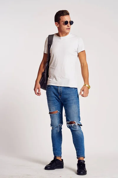 Een man met een rugzak op zijn rug in jeans t-shirt full length sneakers en bril op zijn gezicht — Stockfoto