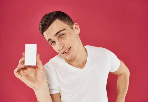 Hombre trabajador con tarjeta de crédito sobre fondo rojo y camiseta blanca vista recortada — Foto de Stock