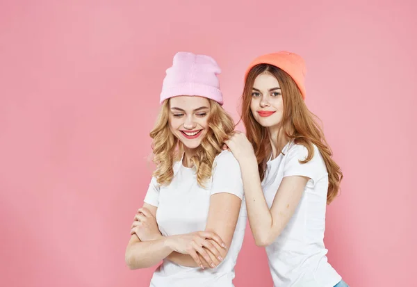 Tişörtlü, renkli şapkalı iki göz kamaştırıcı kız arkadaş iletişim pembe arka plan — Stok fotoğraf
