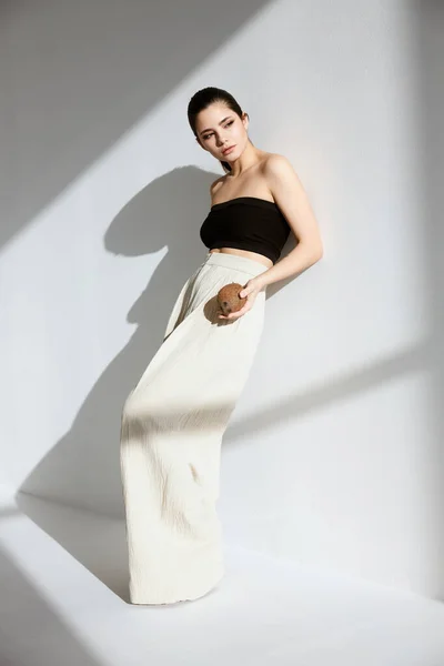 Bela mulher em um top curto e calças brancas perto da parede — Fotografia de Stock
