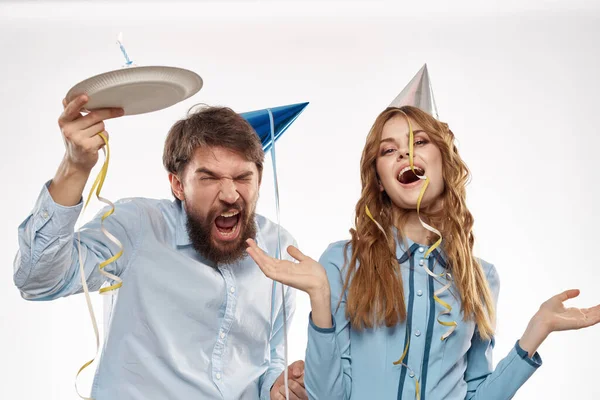 Hombre y mujer enérgicos con un pastel y en sombreros celebran un cumpleaños sobre un fondo claro — Foto de Stock