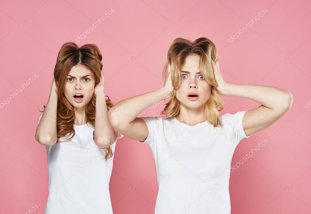 two young girlfriends in white t-shirts cropped view pink background