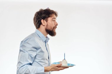 Sakallı bir adam arka planda hafif bir doğum gününde elinde pasta tutuyor.