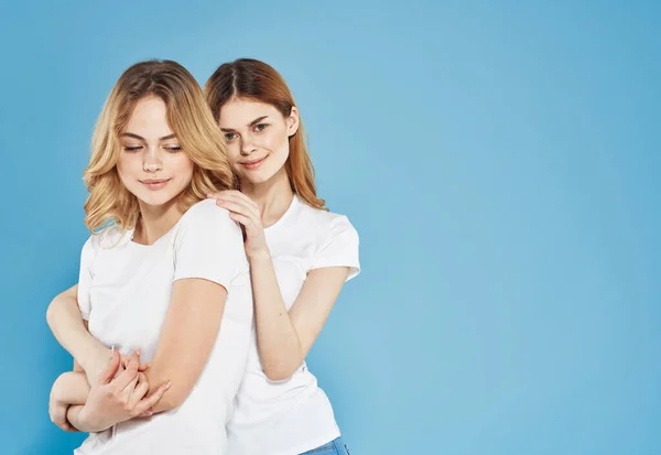 Zwei Freundinnen weißes T-Shirt umarmt Lifestyle-blauer Studiohintergrund — Stockfoto