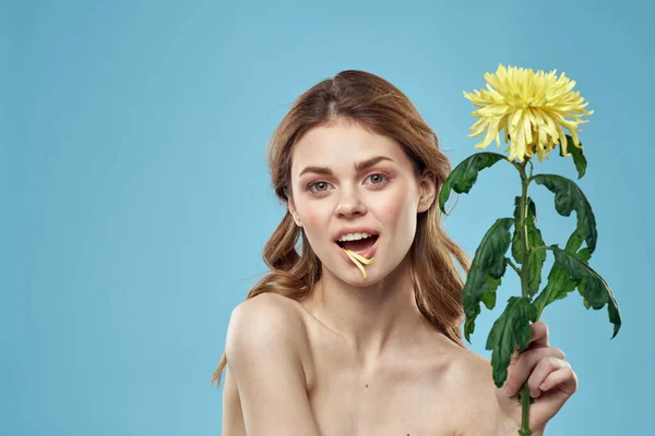 Piękna kobieta z żółtym kwiatem w pobliżu twarzy uśmiechnięty przycięty widok portret nagie ramiona — Zdjęcie stockowe