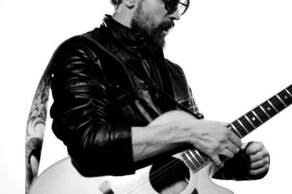 A man plays the guitar in a black leather jacket with sunglasses on a light background — Stock Photo, Image