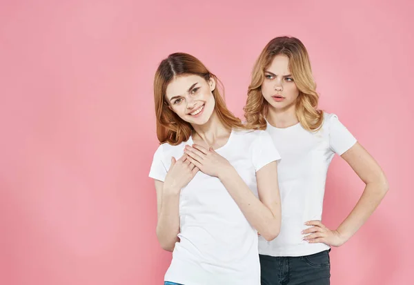 Mujeres alegres en camisetas blancas abrazos socializar estilo de vida Glamor fondo rosa —  Fotos de Stock