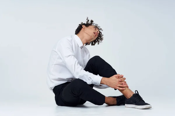 Homem com cabelo encaracolado em um terno clássico e tênis senta-se no chão e vista lateral Espaço Copiar — Fotografia de Stock