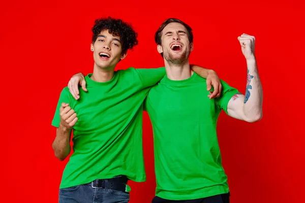 Dos amigos alegres abrazan verde camisetas emociones comunicación fondo rojo — Foto de Stock