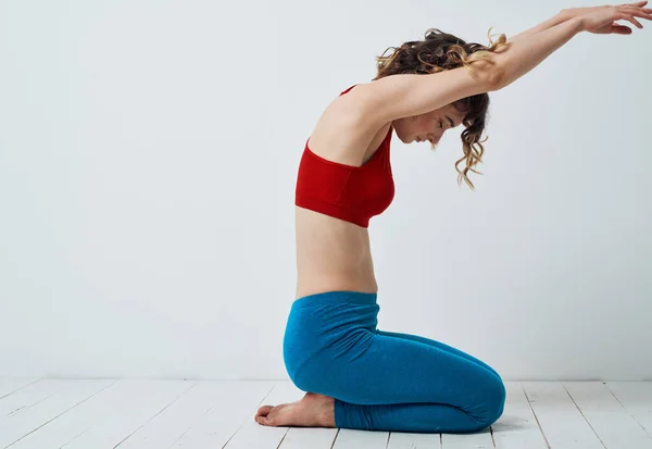 Štíhlá žena ukazuje cvičení na jógu ve světlé místnosti, sedící na podlaze s rukama nad hlavou — Stock fotografie