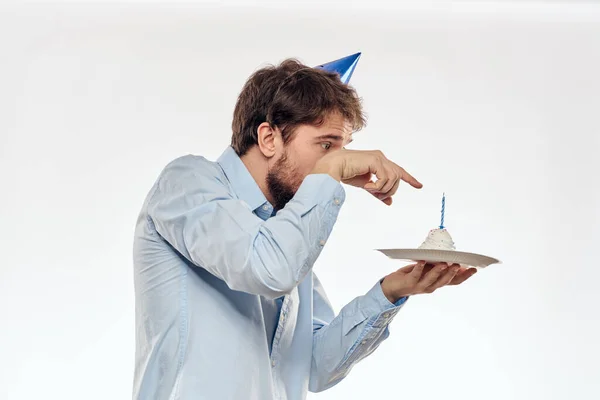 Un homme célèbre un anniversaire sur un fond clair avec un gâteau dans une plaque flûte chapeau amusant — Photo
