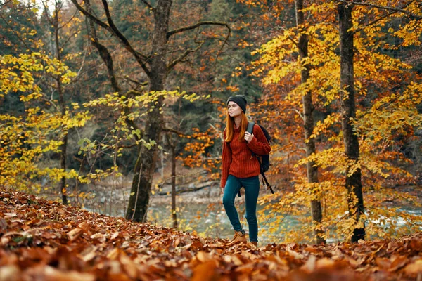 Mulher turista caminha pelo parque no outono com uma mochila em suas costas e árvores altas paisagem rio lago — Fotografia de Stock