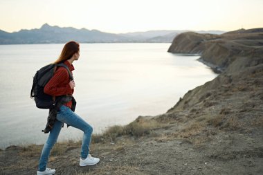 Kadın deniz kenarındaki dağlarda dinleniyor ve sırt çantasıyla turizm modeline biniyor.