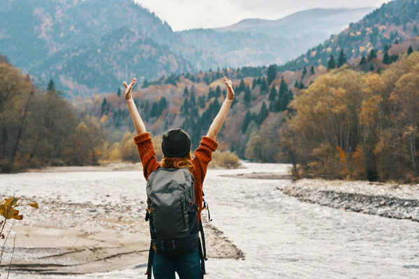 happy traveler gesturing with her hands on the river bank in the mountains