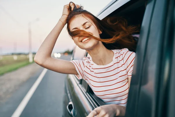 Enérgico vermelho-haired t-shirt mulher espreitando para fora da janela do carro aberto na estrada trilha viagem — Fotografia de Stock