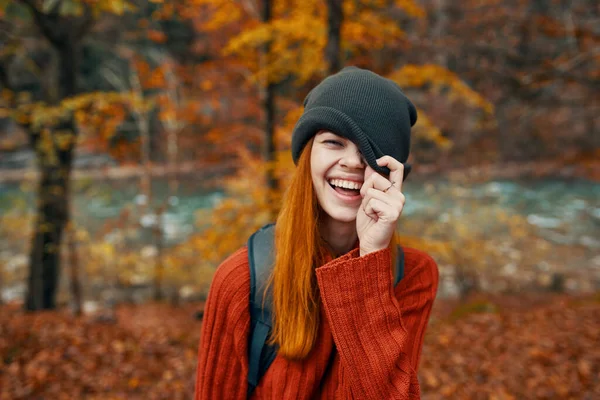 头戴帽子，背着背包，身穿毛衣的女人，秋天风景秀丽的河流 — 图库照片