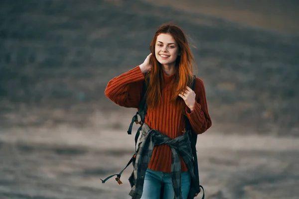 red-haired woman hiker resting in the mountains in nature with a backpack on her back