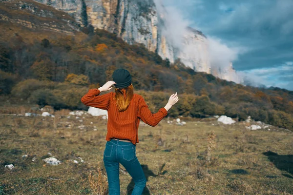Žena ve svetru drží ruce za hlavou a dívá se na vysoké hory krajina modrá obloha mraky — Stock fotografie