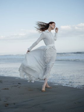 Okyanusun yanındaki beyaz elbiseli kadın çıplak ayak portresi.