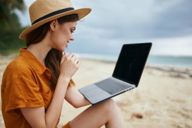 Adanın sahil sahilinde dizüstü bilgisayarı açık serbest çalışan bir kadın.