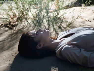 Güzel bir kadın açık havada kumsalda uzanır.