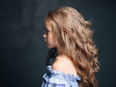 Kıvırcık saçlı, esmer, çıplak omuzlu ve mavi elbisesi olan güzel bir kızın portresi.