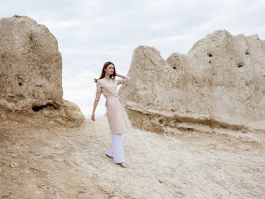 Açık renk elbiseli ve pantolonlu kadın kayalıkların yanında.