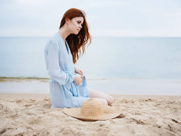 Una donna vestita di blu sulla sabbia e un cappello in mano al mare dell'oceano — Foto Stock