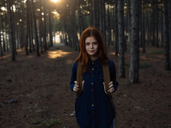 Sırtında sırt çantasıyla çam ormanında mavi gömlekli kızıl saçlı bir kadın. — Stok fotoğraf