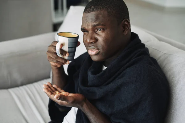 Hombre africano con una taza y pastillas en las manos problemas de salud —  Fotos de Stock