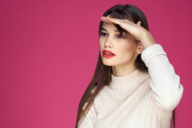 Uzun saçlı esmer, kırmızı dudaklı, kozmetik, beyaz süveter, pembe arka plan kırpık manzaralı.