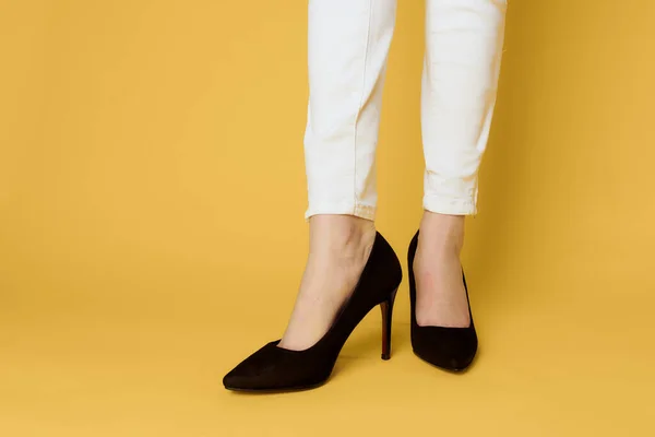 Piernas femeninas zapatos negros moda atractivo look blanco jeans fondo amarillo — Foto de Stock