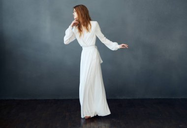 Beyaz elbiseli güzel bir kadın, gri bir arka planda, tamamen büyümüş bir şekilde yere uzanıyor.