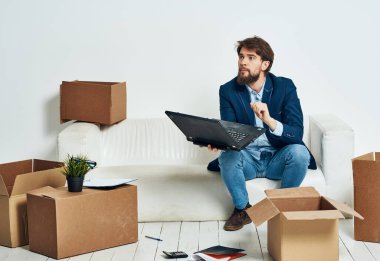 Laptop ofis kutularıyla kanepede oturan bir adam.