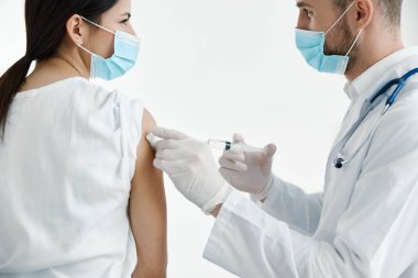 Beyaz önlüklü doktor bir kadına omuz aşısı yapıyor. Hastanedeki kadın hastaya koruyucu eldiven takıyor.