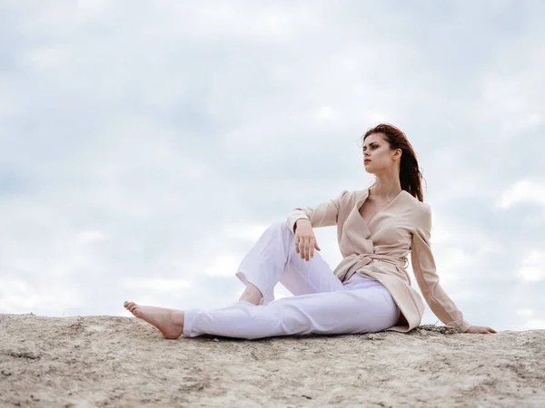 Une femme en vêtements légers est assise sur le sable près de l'océan dans la nature — Photo