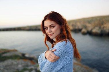 Açık havada kazak giyen kızıl saçlı güzel bir kadın kayalık dağlarda tatil yapıyor.